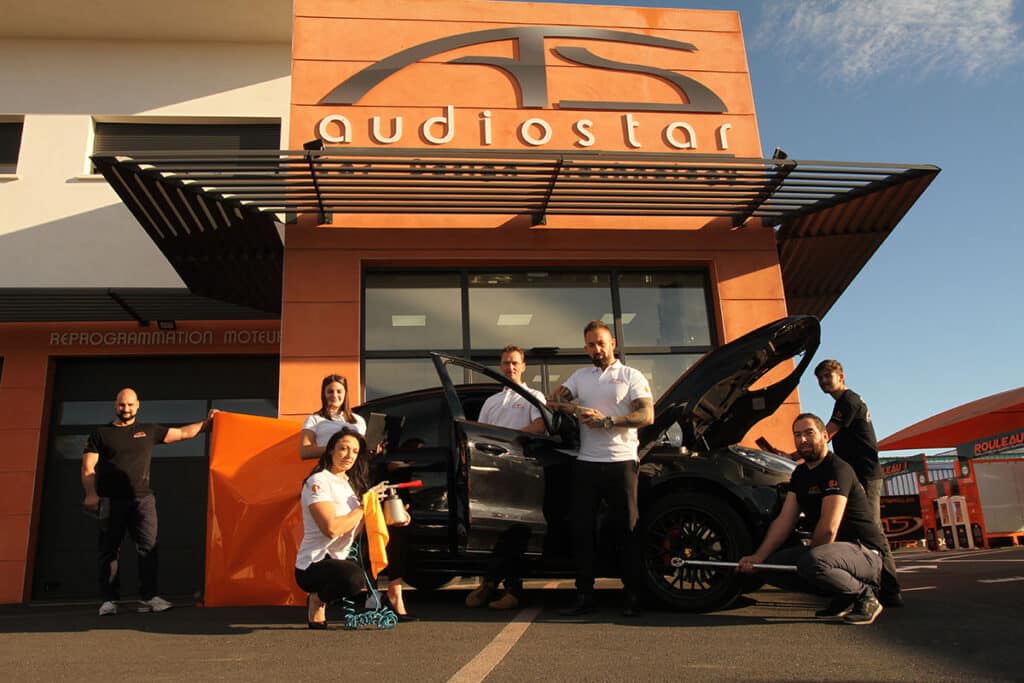 Audiostar : équipe devant bâtiment, logo, Reprogrammation Moteur. Staff près voiture noire, travaux.